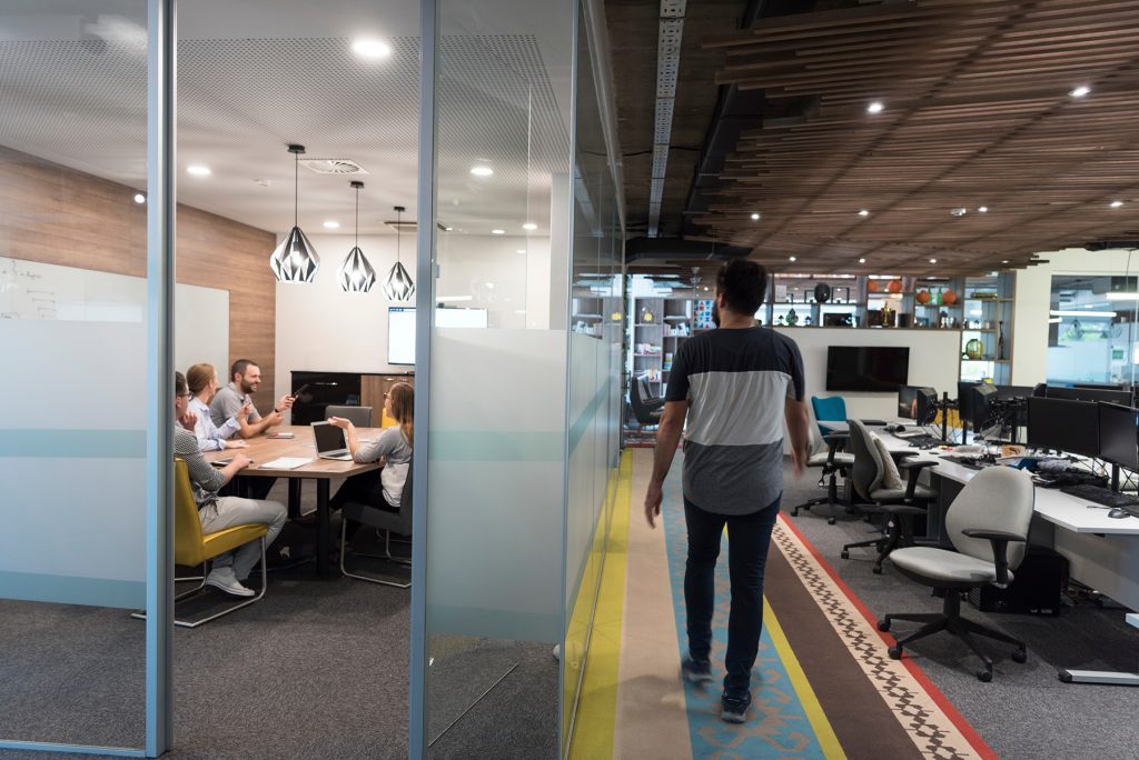 Team members brainstorming in a conference room and a man outside it walking by.